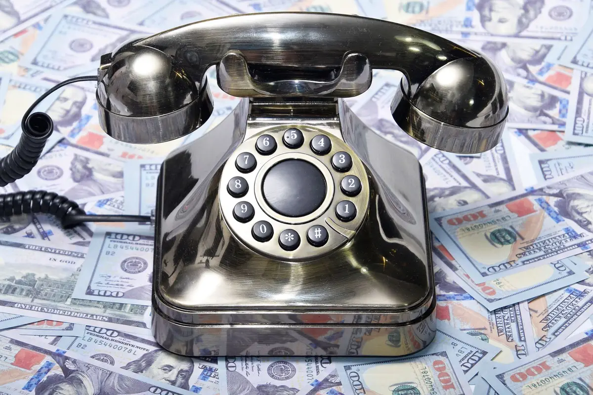 Old telephone resting on a pile of US dollar bills