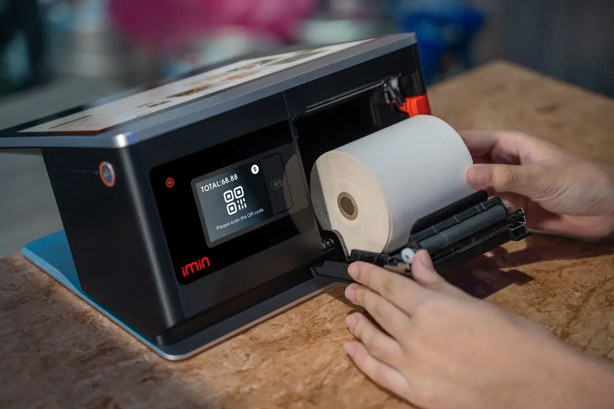 Hands loading receipt paper into a point-of-sale terminal