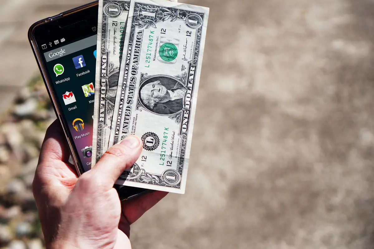 Hand holding dollar bills next to a phone